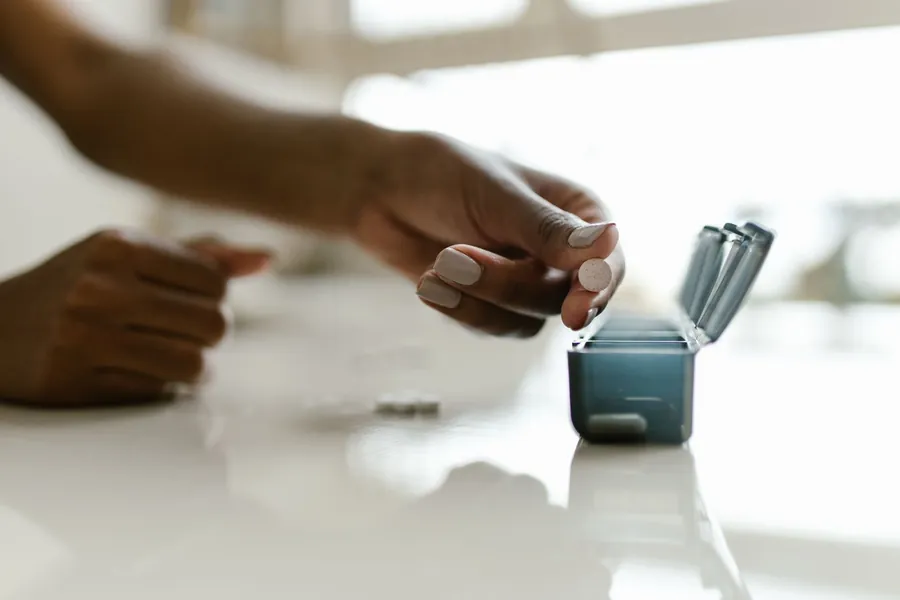 A hand filling a weekly pill organizer on a table.